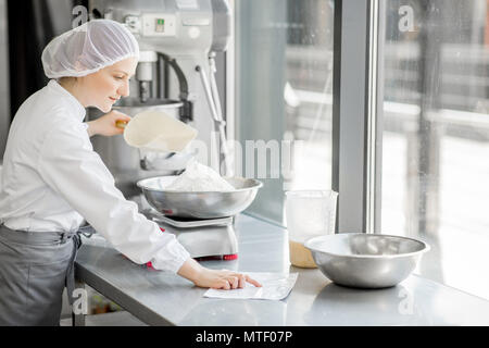 Frau Konditor in Uniform wiegen Zutaten für Gebäck in der Bäckerei verarbeitenden Gewerbe Stockfoto