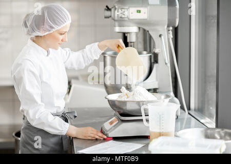 Frau Konditor in Uniform wiegen Zutaten für Gebäck in der Bäckerei verarbeitenden Gewerbe Stockfoto