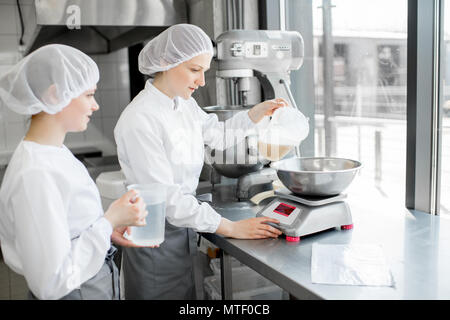 Zwei weiblichen Konditoren in Uniform wiegen Zutaten für Gebäck in der Bäckerei verarbeitenden Gewerbe Stockfoto