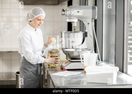 Frau Konditor in Uniform wiegen Zutaten für Gebäck in der Bäckerei verarbeitenden Gewerbe Stockfoto