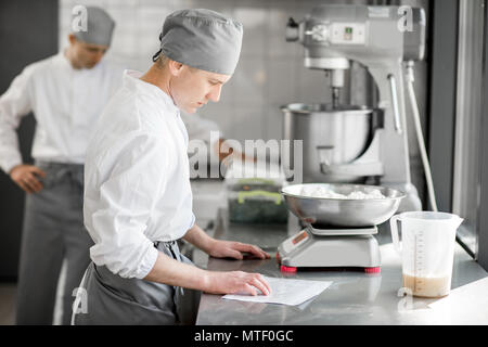 Zwei stattliche männliche Konditoren in Uniform wiegen Zutaten zum Backen in der Fertigung Stockfoto