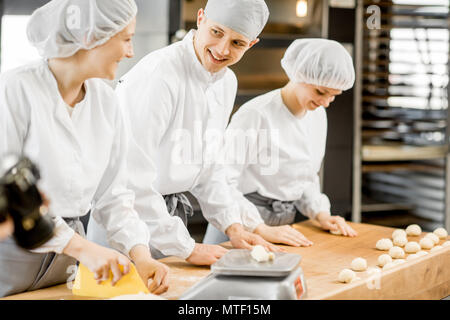 Drei Bäcker Spaß bilden Teig zum backen zusammen, der auf die moderne Fertigung Stockfoto