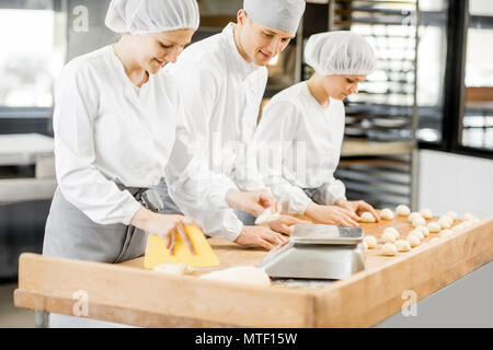 Drei Bäcker Spaß bilden Teig zum backen zusammen, der auf die moderne Fertigung Stockfoto