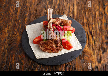 Ribeye Steak auf den Knochen, Tomahawk, serviert mit Tomaten und Eisbergsalat auf pita auf Schiefer. Stockfoto