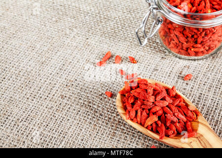 Getrocknete Goji Beeren auf einem Löffel aus Holz und Glas auf Leinen Hintergrund, selektive konzentrieren. Stockfoto