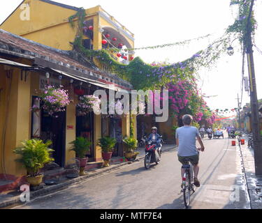 HOI AN, VIETNAM - 20. MÄRZ 2018: Zurück von einem Mann reiten Fahrrad und Mädchen mit Panda Maske auf Motorrad am frühen Morgen in Hoi An Stockfoto