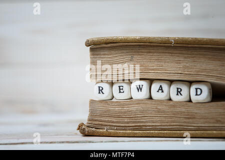 Wort Belohnung in Holz- Bausteine im Buch auf weiße Holztisch geschrieben Stockfoto