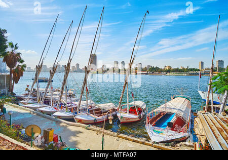 Kairo, Ägypten - Dezember 24, 2017: Der Yacht Club an der Corniche El Nil in Downtown, traditionelle feluccas Rocken auf den Wellen mit Gizeh Stadtbild auf Stockfoto
