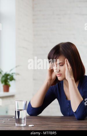 Junge Frau mit starken Kopfschmerzen, die erntehaltefinger zu ihrem Tempel und schließen die Augen vor Schmerz, prepairing Medizin. schwere Migräne.asp Stockfoto