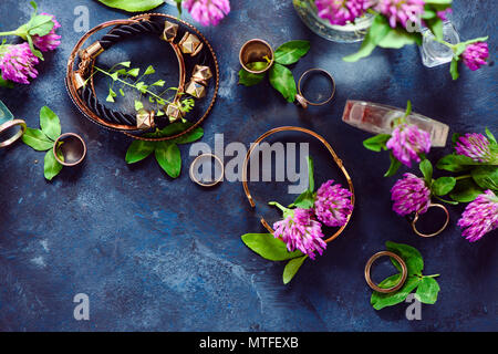 Goldene Armbänder und Ringe in einem femininen Stil Konzept mit Klee Blumen auf einem dunklen Hintergrund. Schönen Sommer Zubehör. Stockfoto