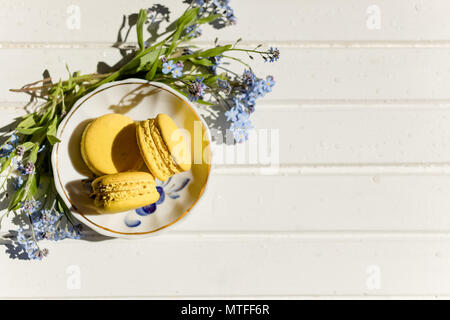 Leckere bunte Makronen auf trendy vintage Holztisch mit vergißmeinnicht Blumen und Konfetti, flach. Lecker gelb, Zitrone Makronen. Platz für Text. candy für die Partei. Getonten Bild Stockfoto