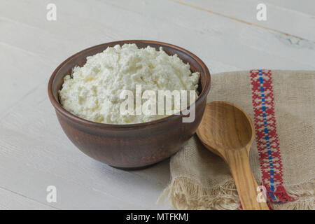 Quark in einem braunen Keramik Schüssel mit authentischen Flachs bestickt Serviette und einem Löffel aus Holz, auf einem weißen Holz- Hintergrund. Anzeigen in einem Winkel. Schließen Stockfoto