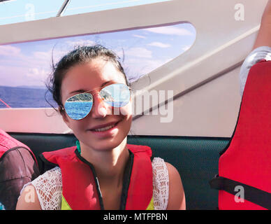 Lächelnd dunkelhaarige Frau Segel auf tropischen Meer Tragen von Schwimmwesten und Sonnenbrillen. Stockfoto