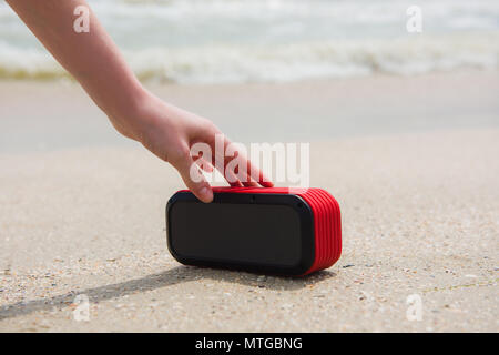 Weibliche hand Touch tragbarer Lautsprecher. Frau und drahtlose USB-akustischen am Strand mit Sand Stockfoto