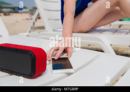 Weibliche hand mit Telefon und Lautsprecher am Strand. Frau genießen Urlaub mit Wireless Bluetooth Gadgets Stockfoto