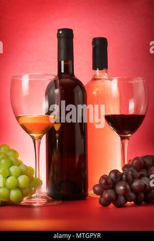 Komposition mit Rot- und Weißwein Flaschen, Traube eine Trinkgläser. Auf rotem Hintergrund Stockfoto