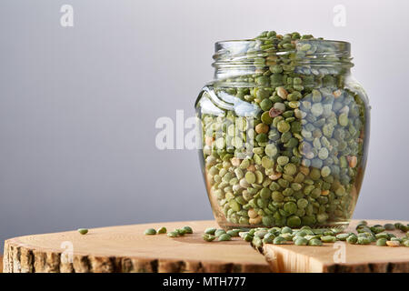 Rohe grüne Erbsen im Glas auf einem Baumstamm über Graues unscharfen Hintergrund, Nahaufnahme, selektiven Fokus. Einige kopieren Sie Raum für Ihre Beschriftung. Studio gedreht. Orgel Stockfoto