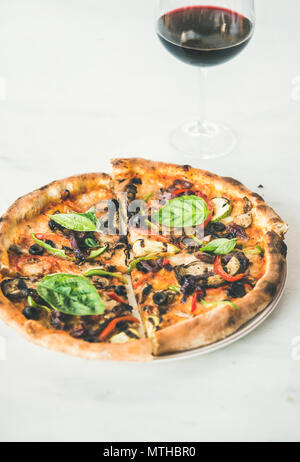 Frisch gebackene Pizza mit Gemüse, Basilikum und Glas Wein Stockfoto