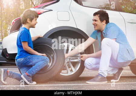 Porträt der glückliche junge Vater und Sohn Räder ändern auf Auto mit reifen Schraubenschlüssel am Parkplatz außerhalb Stockfoto