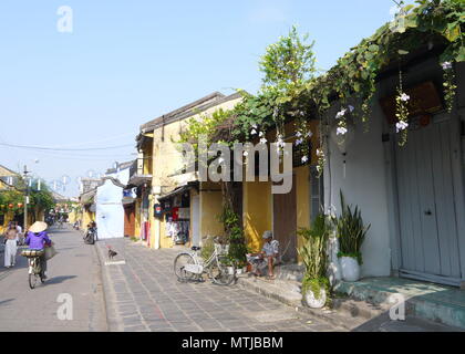 HOI AN, VIETNAM - 17. MÄRZ 2018: ein Mann sitzt auf einem Schritt vor einem closed shop lesen Zeitung frühe sonniger Morgen in Hoi An Stockfoto