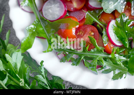 Auf dem Tisch auf einem weißen Teller Salat, Radieschen, Tomaten, Rucola. In der Nähe vorgestellt. Die Aussicht von oben. Stockfoto