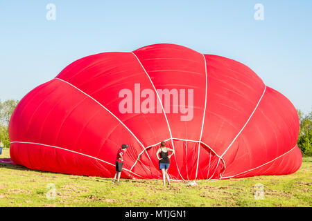 Zuschauer verfolgen als rote Jungfrau Hot Air Balloon bläst sich auf Lyndon Top, Rutland Water, England. Stockfoto