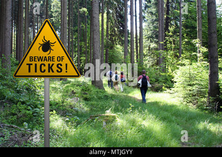 Warnschild "Vorsicht vor Zecken" in befallenen Gegend im grünen Wald mit Strohschüttler Stockfoto