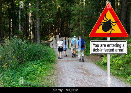 Warnschild "Vorsicht vor Zecken" in befallenen Gegend im grünen Wald mit Wanderer Stockfoto