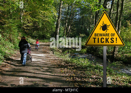 Warnschild "Vorsicht vor Zecken im befallenen Bereich in einem Park mit Wandern Familie Stockfoto