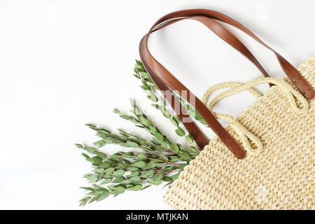 Styled Foto. Feminine Stilleben Komposition mit Stroh Französisch Warenkorb Tasche mit langen ledergriffen und Eukalyptus Niederlassungen auf weißem backgouns, Stockfoto