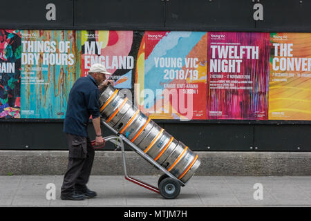 Eine drayman in London liefern Aluminium Behälter und Fässer Bier oder Ale in einer Kneipe oder Cafe vor einige bunte Werbetafeln. Sackkarre in Ale Stockfoto