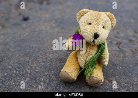 Ansicht von oben wenig brauner Bär Puppe tragen grüne Schal mit lila Blüte in Grauen Asphalt Sitzen Stockfoto