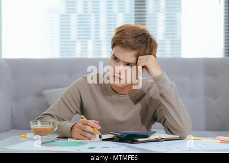 Junge attraktive junge asiatischer Mann zu Hause auf dem Sofa sitzen mit Rechner Rechnungswesen Kosten, Gebühren, Steuern und Hypothek für das Bezahlen von Rechnungen suchen Sonnenliegen Stockfoto