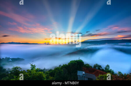 Dämmerung auf der Hochebene am Morgen mit bunten Himmel, während die Sonne vom Horizont scheint Steigende, kleines Dorf mit Nebel eingehüllte Landschaft Stockfoto
