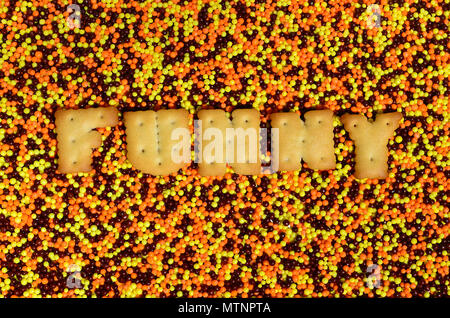 Lustig. Das Wort von den essbaren cracker Buchstaben liegt auf der verglasten Pulver. Eine große Anzahl von süßen, bunten Perlen von sehr kleinen Größe für die Dekoration o Stockfoto