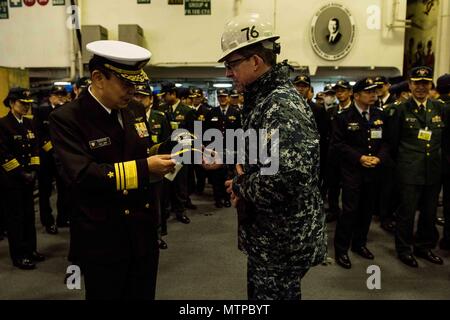 180123-N-OY 799-060 Yokosuka, Japan (Jan. 23, 2018) Kapitän Buzz Donnelly, kommandierender Offizier der Marine vorwärts - bereitgestellt Flugzeugträger USS Ronald Reagan (CVN 76), Austausch Geschenke mit Vice Adm. Katsuto Deguchi, Kommandant, Joint Staff College, während einer Tour im Hangar Bay. Ronald Reagan, das Flaggschiff der Carrier Strike Group 5, bietet eine Bekämpfung bereit, Kraft, schützt und verteidigt die kollektive maritime Interessen seiner Verbündeten und Partnern in der Indo-Asia-Pazifik-Region. (U.S. Marine Foto von Mass Communication Specialist 2. Klasse Kenneth Abbate / freigegeben) Stockfoto