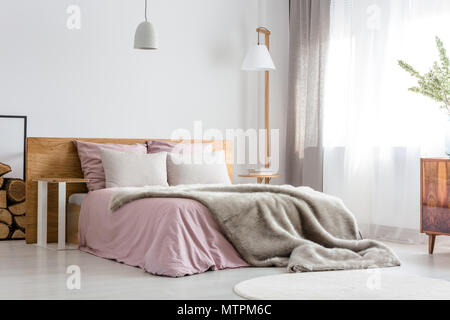 Flauschige graue Decke auf Bett aus Holz mit rosa Bettwäsche Stockfoto