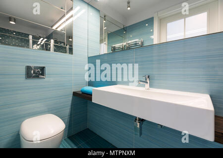 Geräumiges Badezimmer mit Waschbecken und wc, blauen Fliesen und Spiegel an der Wand Stockfoto