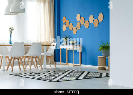 Modernen stilvollen Speisesaal mit blauen Wand, Holztisch, weißen Stühlen, gemusterten Teppich, Fenster- und Kork Stockfoto