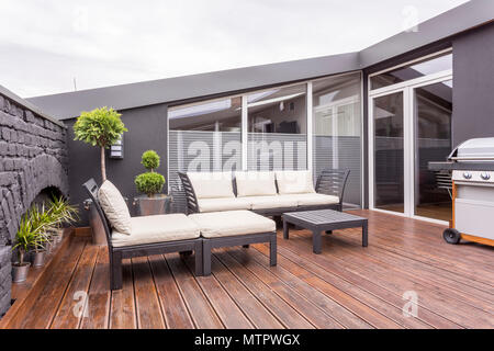 Solarium, Garten Sofa und Couchtisch auf Holzboden von einfachen Terrasse mit Grill und Wand Stockfoto