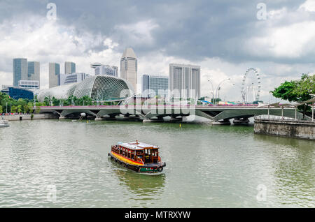 Eine Kreuzfahrt Boot wie die twakows Fahrt durch die berühmten Singapore River bekannt. Das Gebäude an der Rückseite ist die berüchtigte Theater an der Bucht, Esplanade. Stockfoto