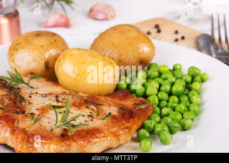 Nahaufnahme von Schweinekotelett, gekochte Kartoffeln und grünen Erbsen auf einem Teller serviert. selektive Fokus Stockfoto