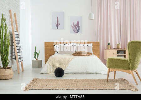 Green retro Stuhl und schwarze Kugel im Schlafzimmer mit Poster an der Wand über Kingsize-Bett und Cactus neben Leiter Stockfoto