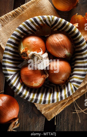 Noch immer leben von Zwiebeln und Knoblauch Kopf in einem Weidenkorb auf einem Sack und Holzplatten. Von oben gesehen. Im rustikalen Stil. Bild vertikal. Stockfoto