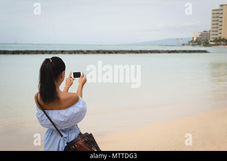 Frau anklicken Foto von Meer mit Handy Stockfoto