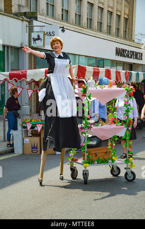 Eine Street Performer in Hammersmith und Fulham Frühling Markt tragen Stelzen und gekleidet als Dienstmädchen oder Kellnerin. Stockfoto