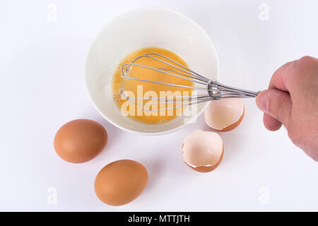 Koch hand mit Schneebesen und Schlagsahne Eier in der Schale auf der weißen Küchentisch. Kochen und Essen Konzept Stockfoto