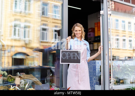 Attraktive junge Frau Blumenhändler in Schürze Holding"-Schild und lächelnd an Kamera Stockfoto