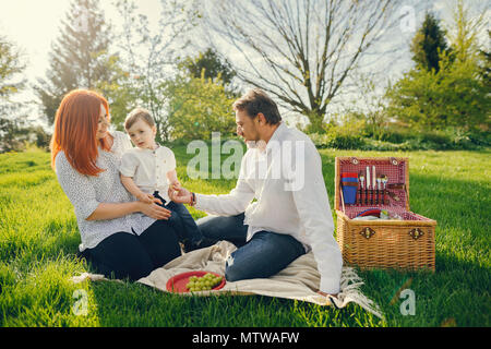 Schöne und stilvolle rothaarige Mama in eine weiße Bluse sitzt im Gras mit ihren schönen Mann in einem weißen T-Shirt und Blue Jeans sie spielen mit. Stockfoto