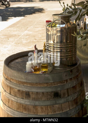 Flaschen aromatisiert Balsamico Essig und Olivenöl Neben einem glänzenden Milchkanne auf einem Holzfass. Stockfoto